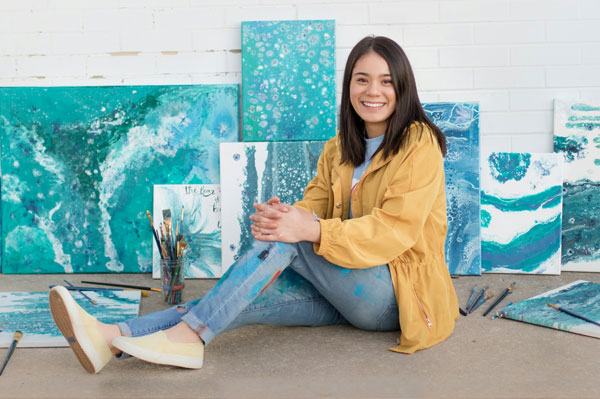 art student sitting in front of her paintings done as part of her art college portfolio projects